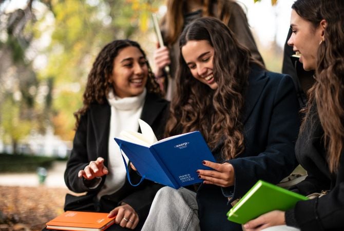 Alumnas en el exterior con libros sonriendo